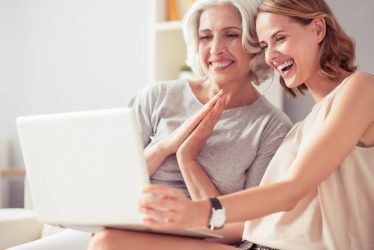 Express your feelings. Cheerful delighted woman and her aged mother sitting on the couch and smiling while using laptop