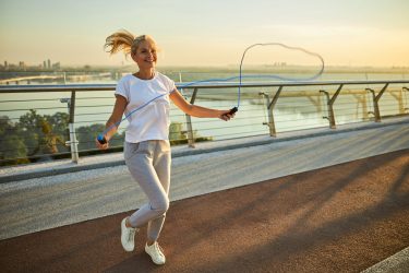 Beautiful smiling lady in sportswear doing exercise with jumping rope on the bridge